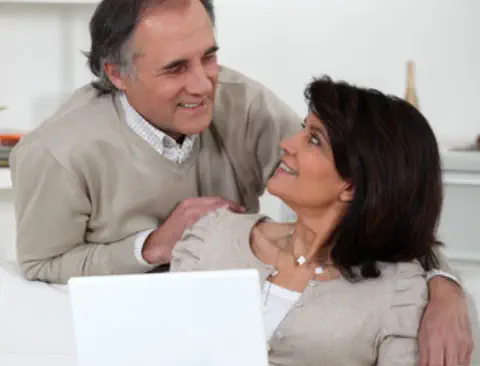 A middle-aged couple are looking at a laptop together in their living room